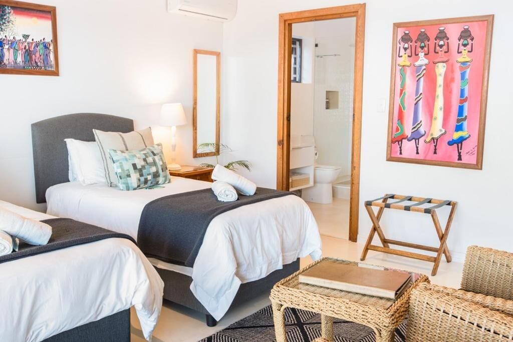 A hotel room with two beds, a small table, a chair, a mirror, and artwork on the walls.