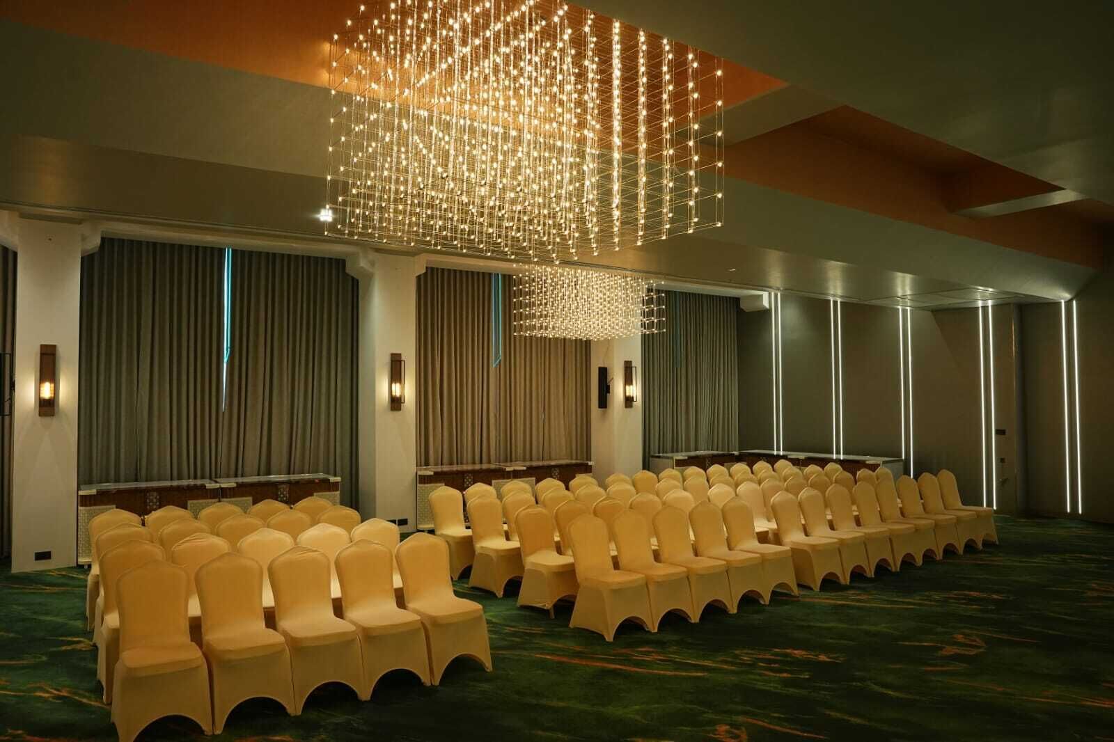 A conference room with rows of chairs, a large chandelier, and a carpeted floor.