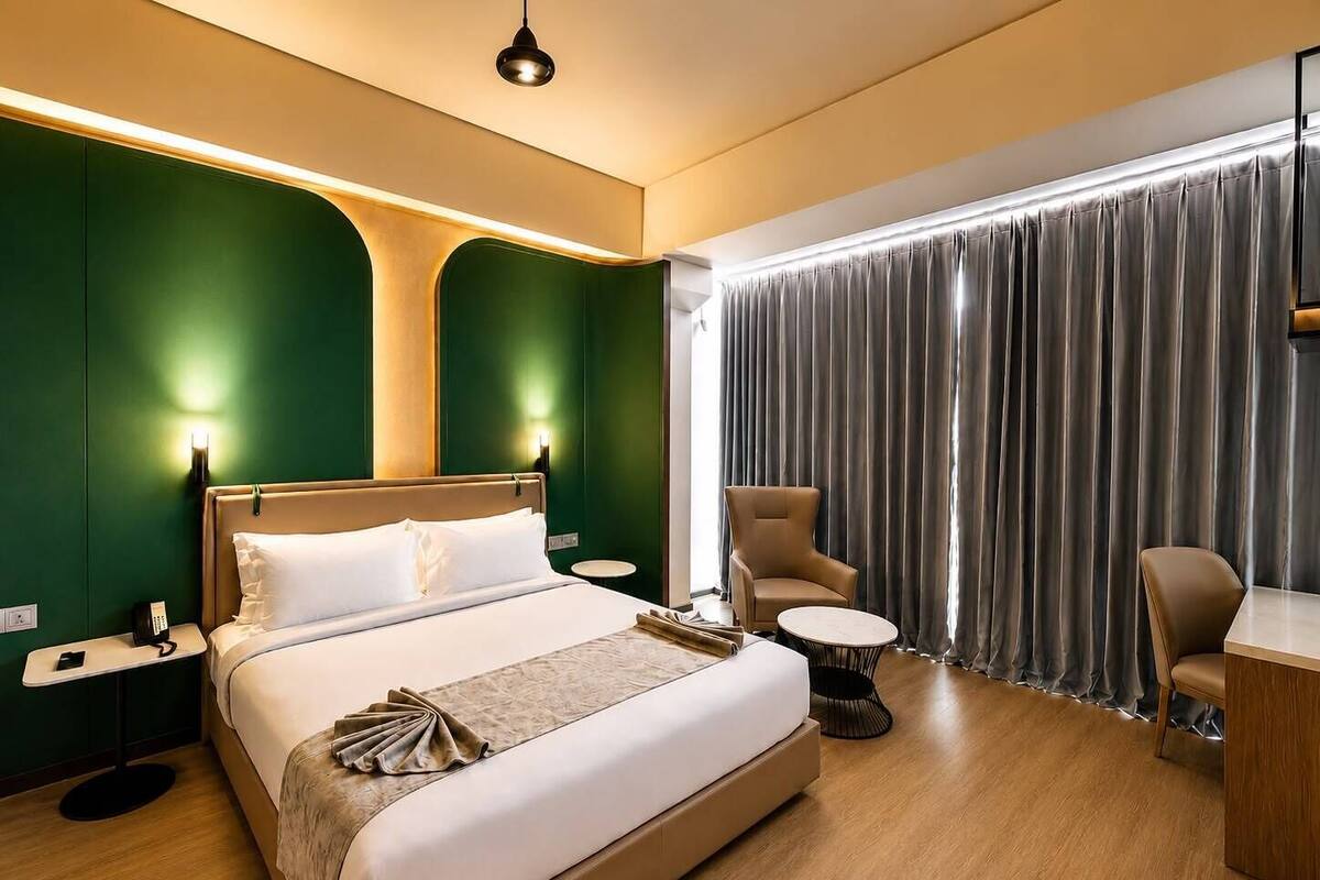 Ein Hotelzimmer mit Bett, Nachttischen, Schreibtisch, Stuhl und einem großen Fenster mit Vorhängen.