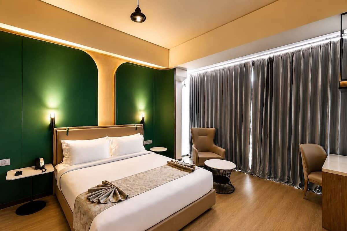 A hotel room with a bed, bedside tables, a desk, a chair, and a large window with curtains.