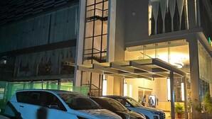 Entrada de hotel com galeria coberta, placa verde e vários carros estacionados.