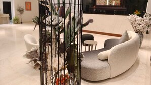 A modern lobby with a seating area, a decorative plant in a metal cage, and a colorful mural in the background. - HOTEL NATANYA (Thanjavur)