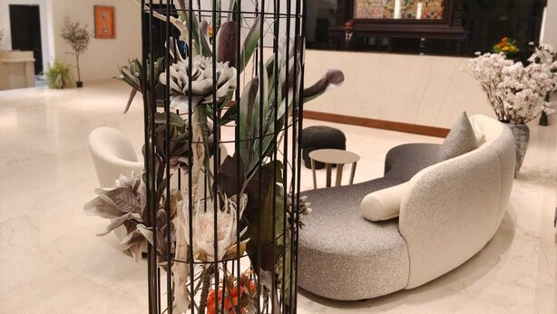 Um lobby moderno com área de estar, uma planta decorativa numa gaiola de metal e um mural colorido ao fundo.