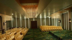 Uma sala de conferências com fileiras de cadeiras, uma mesa comprida e um candelabro.