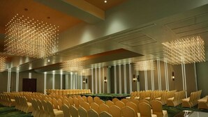 Uma sala de conferências com fileiras de cadeiras, uma mesa comprida e luminárias modernas.