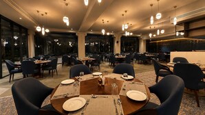 Uma sala de jantar espaçosa com várias mesas, cadeiras e iluminação pendente.