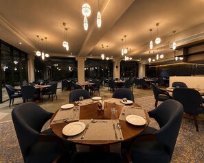 Un vaste espace dédié à la salle à manger, comprenant plusieurs tables, des chaises et des luminaires suspendus.