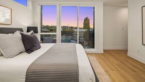 Ein Schlafzimmer mit einem großen Bett, Blick durch eine Schiebetür auf die Stadtlandschaft.