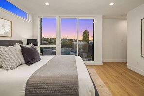 Ein Schlafzimmer mit einem großen Bett, Blick durch eine Schiebetür auf die Stadtlandschaft.