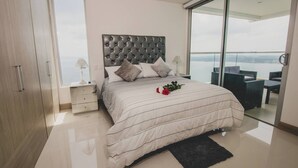 Une chambre moderne avec un grand lit, une table de chevet, une commode et un balcon aménagé avec du mobilier d’extérieur.