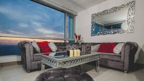 Un salon avec un canapé gris, une table basse en verre et une grande fenêtre donnant sur un beau paysage.