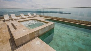 Une piscine à débordement située sur le toit, avec une eau cristalline, un jacuzzi et des chaises longues.