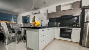 Une cuisine moderne avec des meubles blancs, un plan de travail noir, des appareils en acier inoxydable et un coin repas avec une chaise grise.