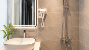 A bathroom with a white sink, a mirror, a hairdryer, and a shower. - Quang Huy Hotel - Trung Phung (Hanoi)