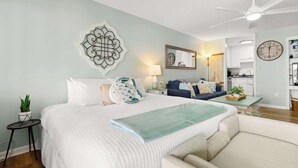 Ein Hotelzimmer mit Bett, Sofa, Esstisch, Lampe, Uhr und einer kleinen Pflanze.