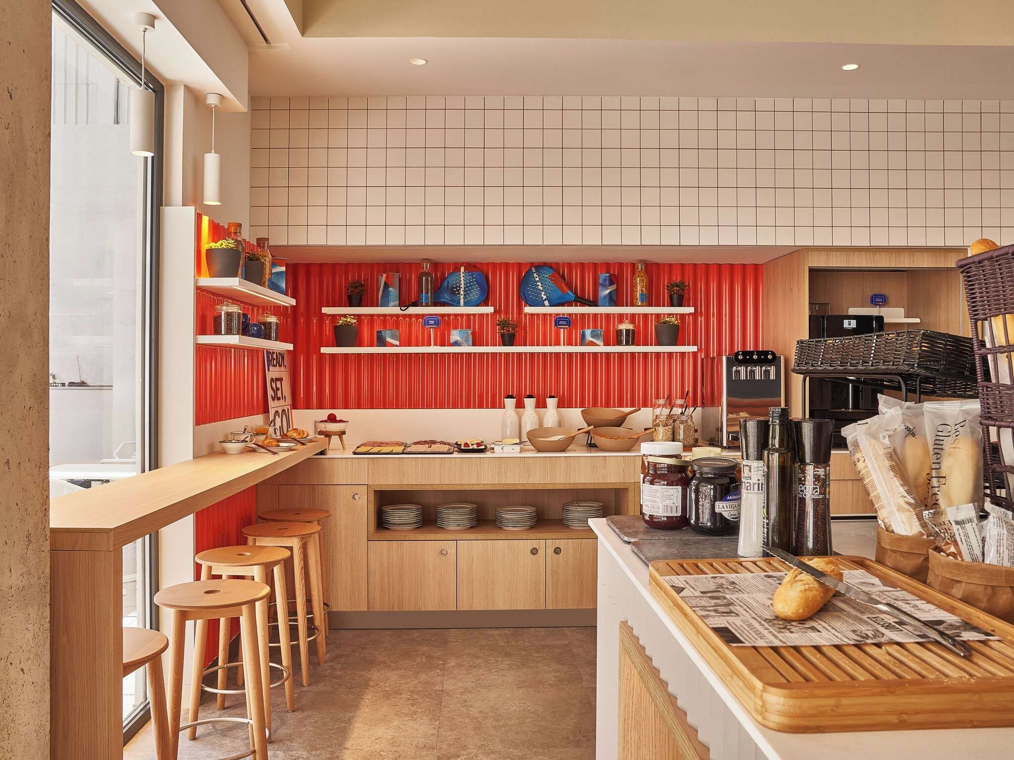Cozinha moderna com bancadas de madeira, banquetas de bar e uma parede com detalhe em vermelho.