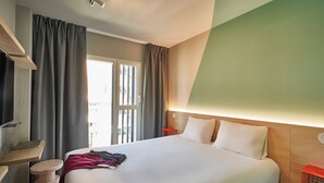 A hotel room with a large bed, a desk, a chair, and a window with curtains. - Ibis Budget Barcelona Center (Barcelona)