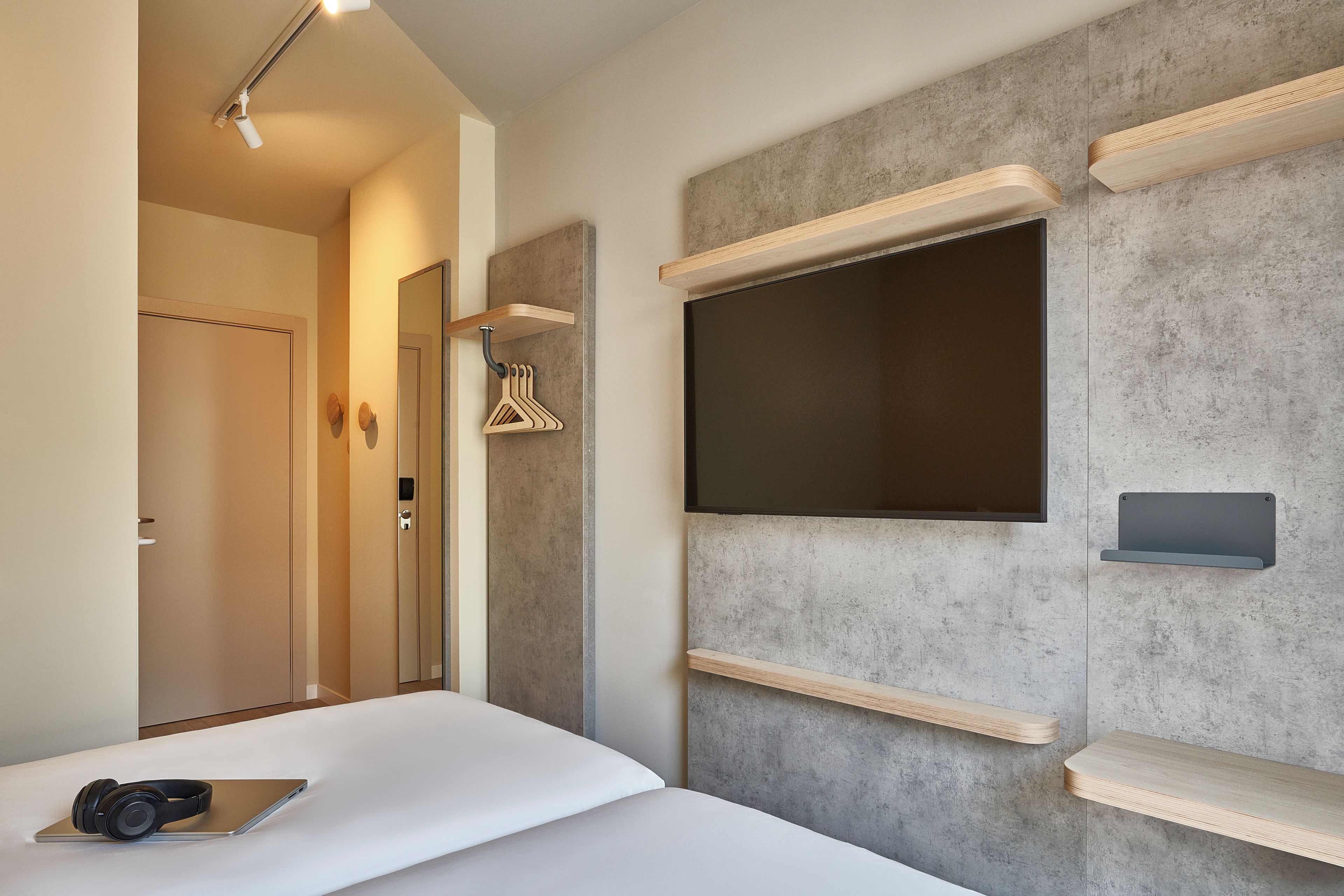 Una habitación de hotel moderna con una cama, un escritorio, un televisor de pantalla plana montado en la pared y una puerta que da a otra habitación.