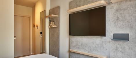 Una habitación de hotel moderna con una cama, un escritorio, un televisor de pantalla plana montado en la pared y una puerta que da a otra habitación.