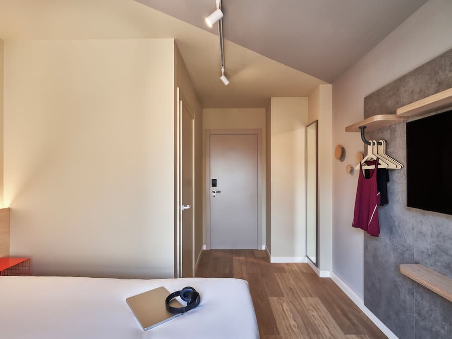 Habitación de hotel con cama, escritorio, televisor montado en la pared y pasillo que conduce a otra habitación.