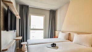 A hotel room with a bed, a small round table, a TV mounted on the wall, and a window with curtains. - Ibis Budget Barcelona Center (Barcelona)