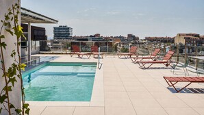 A rooftop pool with clear blue water, surrounded by red lounge chairs and a glass railing. - Ibis Budget Barcelona Center (Barcelona)