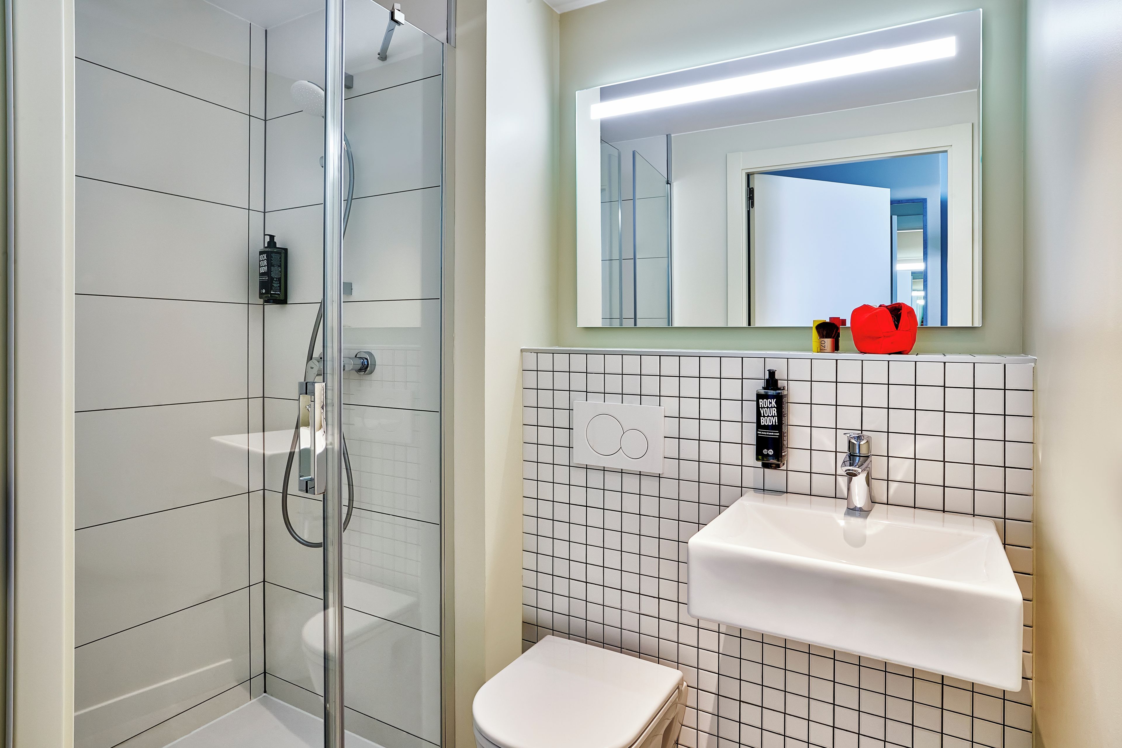 A modern bathroom with a glass-enclosed shower, a white sink with a mirror above it, and a toilet.