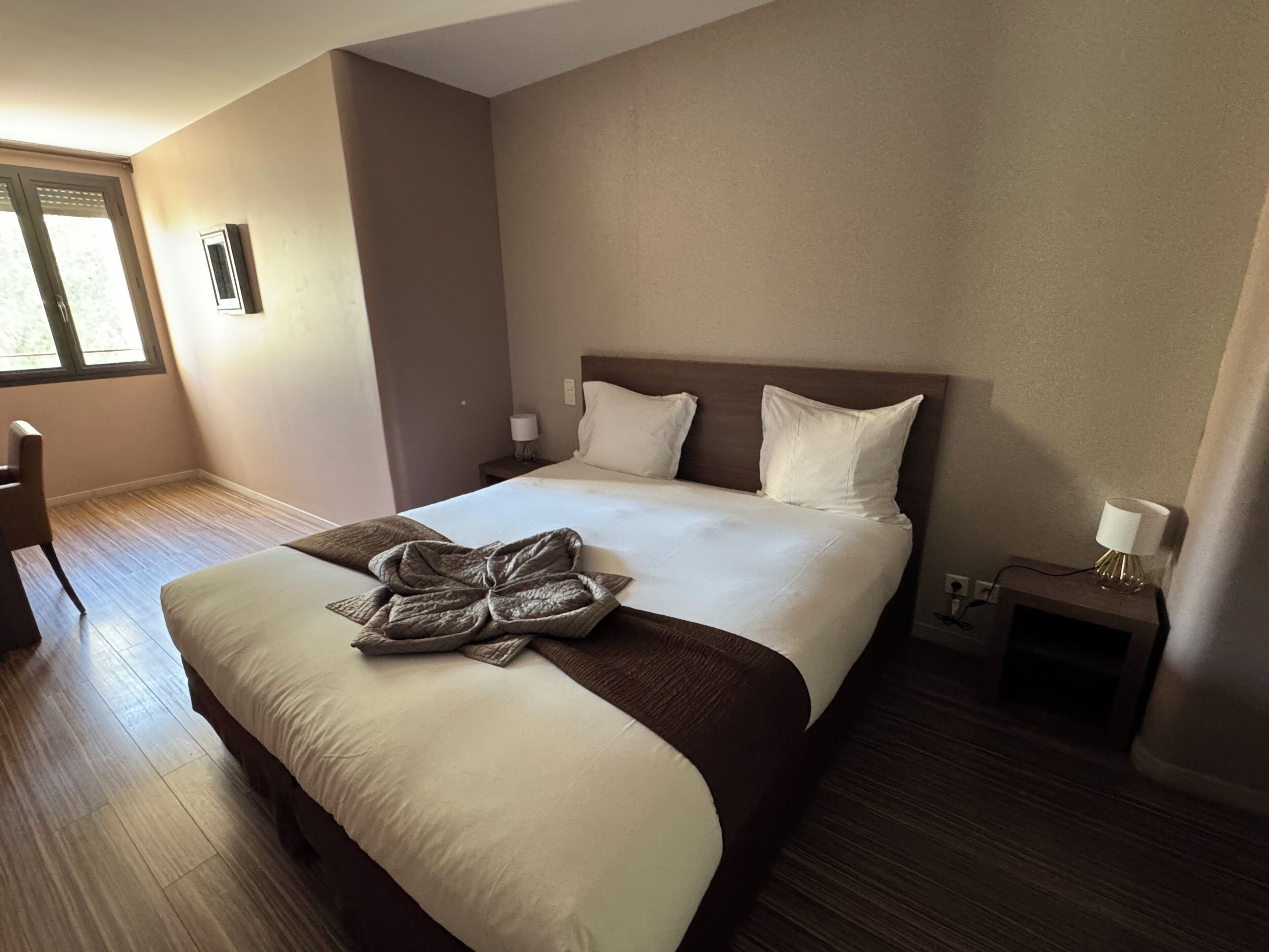 A hotel room with a large bed, a nightstand, a lamp, and a window.