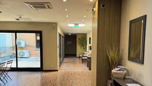 A hotel lobby with a wooden floor, a reception desk, a plant, and a large mirror. - La Bourse (Bagnols-sur-Cèze)