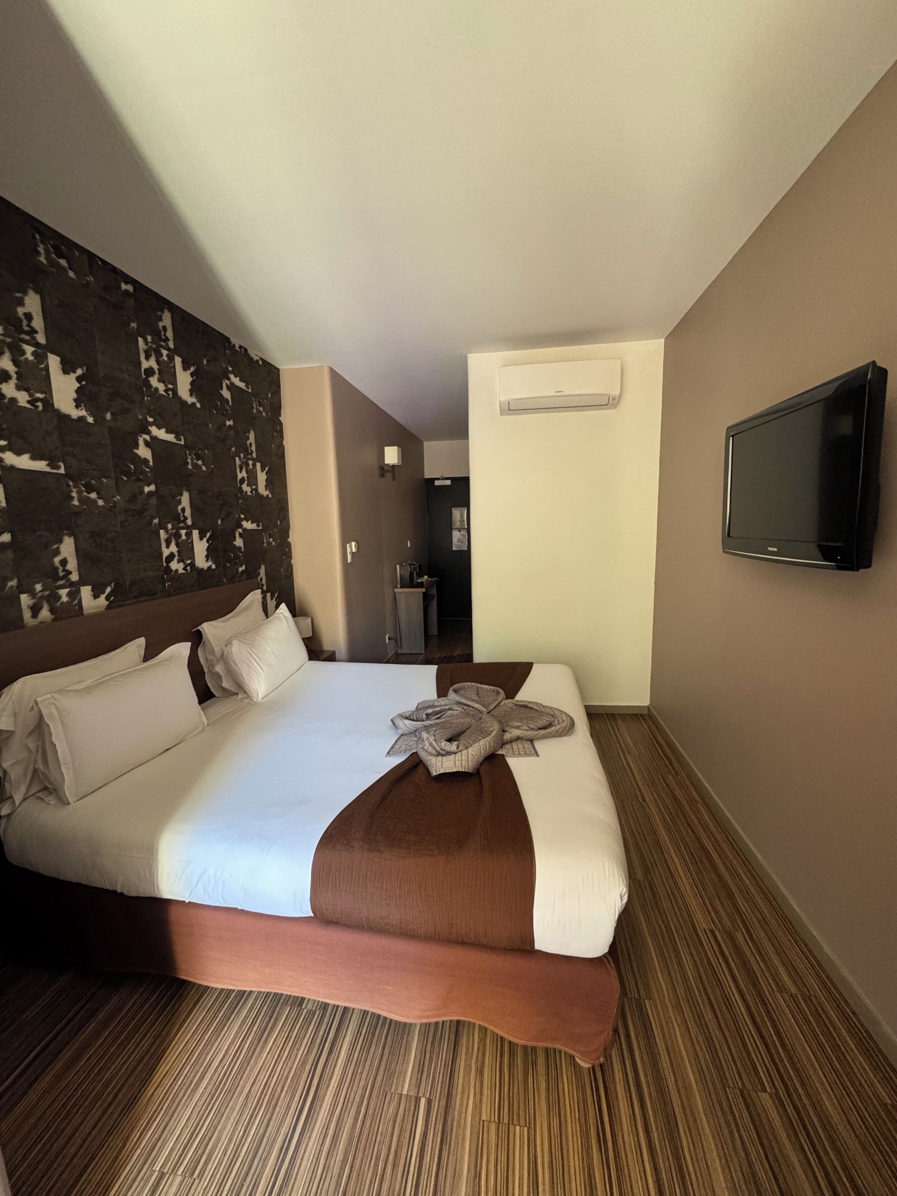 Habitación de hotel con una cama grande, televisión de pantalla plana, aire acondicionado y pared con diseño.