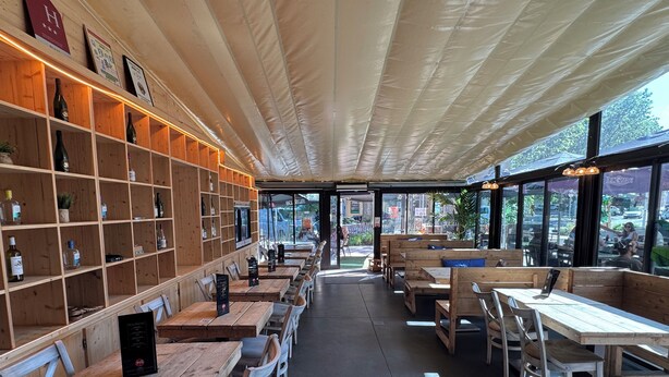A restaurant interior with wooden tables and chairs, a wall with shelves of bottles, and large windows. - La Bourse (Bagnols-sur-Cèze)
