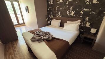 Habitación de hotel con una cama grande, suelo de madera, vista a través de un ventanal y pared con diseño.