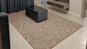 Una sala de estar moderna con un televisor de pantalla plana montado en la pared, un sofá oscuro, una mesa de centro y una alfombra estampada.