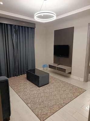 A modern living room with a flat-screen TV mounted on the wall, a dark sofa, a coffee table, and a patterned rug.
