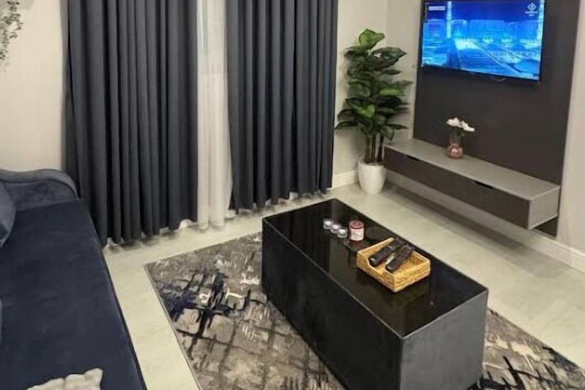 Ein modernes Wohnzimmer mit einer Couch, einem schwarzen Couchtisch, einem an der Wand befestigten Fernseher und einer Zimmerpflanze.