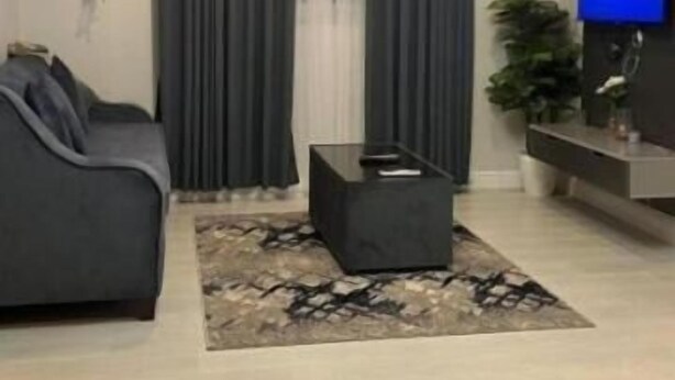 Una sala de estar moderna con un sofá, una mesa de centro, un televisor y un amplio ventanal con cortinas.