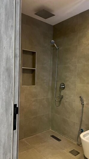 Een douche met een handdouche, een wandmengkraan en een klein plankje.