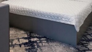 Una habitación de hotel moderna con cama, mesita de noche, lámpara, equipo de aire acondicionado e iluminación circular.