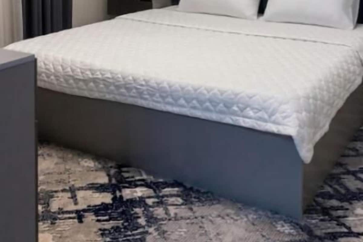 Ein modernes Hotelzimmer mit Bett, Nachttisch, Lampe, Klimaanlage und einer runden Deckenleuchte.