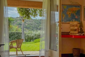Ein Zimmer mit Blick auf eine üppige grüne Landschaft, ein Korbstuhl, ein Globus an der Wand und ein rotes Regal mit Dekoration.