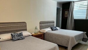 Duas camas de solteiro com cabeceiras listradas, uma mesa de cabeceira com abajur e uma janela com cortinas.