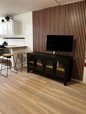 A modern living space with a wooden panel wall, a black entertainment unit, and a dining area with stools. - Private Isabela 2-bedroom Apt. near Park, Plaza & Beaches (Isabela)