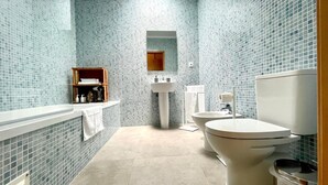 A bathroom with a tiled wall, a sink, a toilet, and a shelf with toiletries.