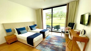 A hotel room with two beds, a desk, a TV, and a view of the outdoors.