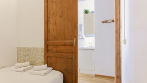 Een slaapkamer met een houten deur, een bed met witte lakens en een zichtbare badkamer door een open deur.