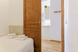 A bedroom with a wooden door, a bed with white linens, and a bathroom visible through an open door. - Gracia, quiet, well-equipped, centrally located 2-bedroom apartment (Barcelona)