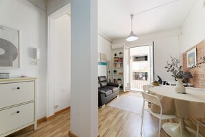 Ein modernes Wohnzimmer mit einer Couch, einem Esstisch mit Stühlen, einer weißen Kommode und einem großen Fenster.