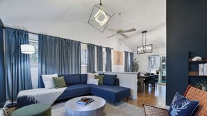 Uma sala de estar moderna com um sofá modular, uma mesa de centro redonda e uma área de jantar ao fundo.
