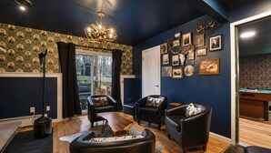 Quarto com mesa de bilhar, poltronas de couro, lustre e quadros nas paredes.