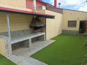 A patio with a built-in grill, a tiled bench, and a small grassy area.